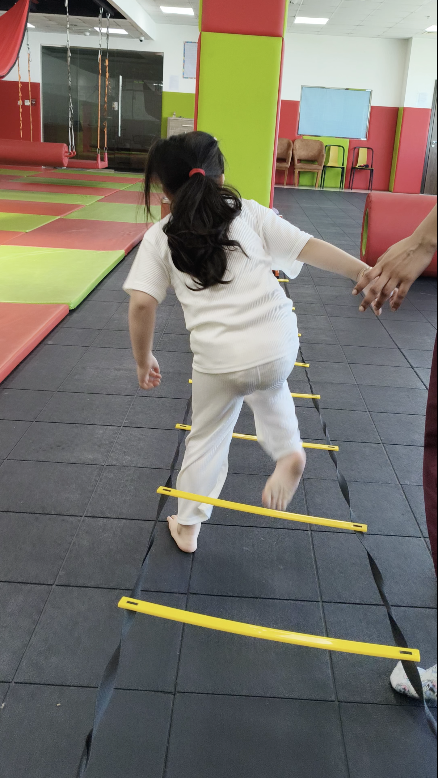 Child practicing ladder walking with therapist support during a gross motor skill activity in a therapy center.